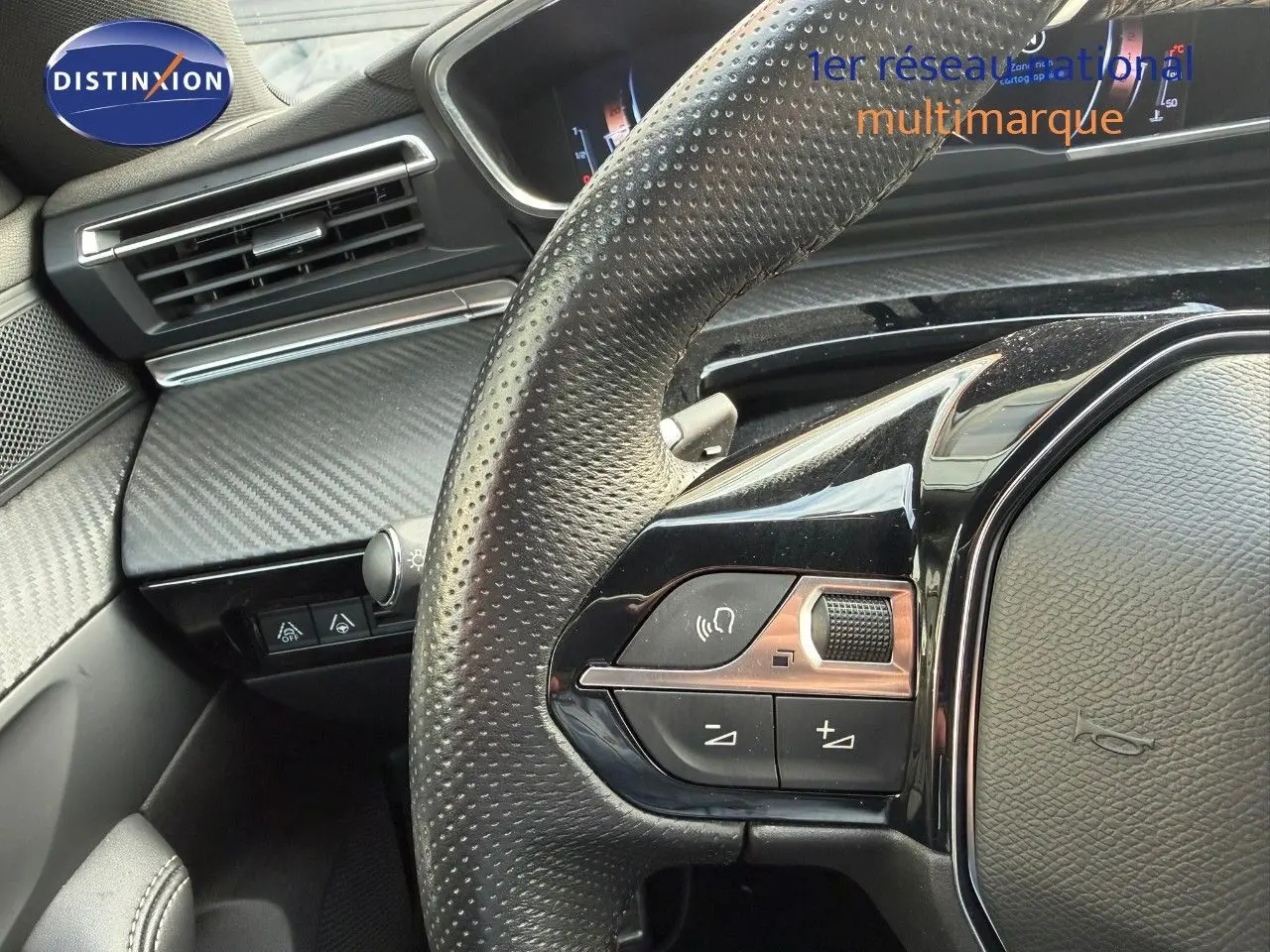 Gros plan sur le volant en cuir perforé côté gauche du Peugeot 508 gris platinium, avec commandes intégrées et tableau de bord partiel.