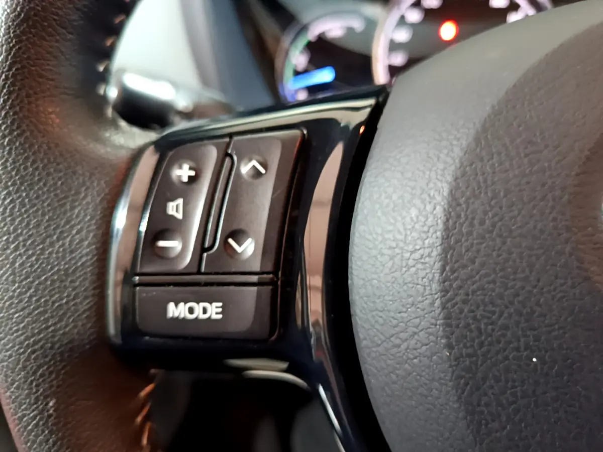 Gros plan sur les commandes du volant noir de la Toyota Yaris hybride blanche, avec boutons de réglage et mode audio.