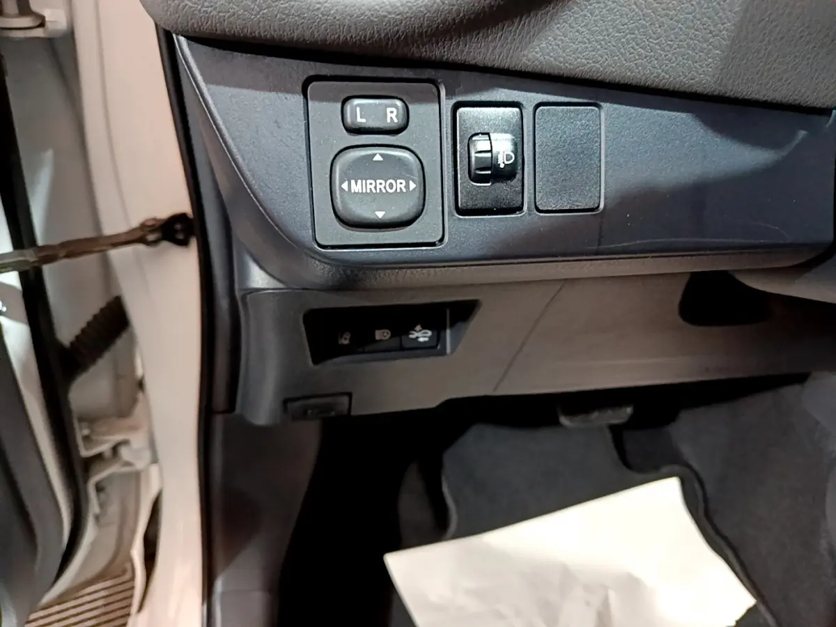 Vue intérieure côté gauche de la Toyota Yaris blanche, montrant les commandes de réglage des rétroviseurs et des phares.