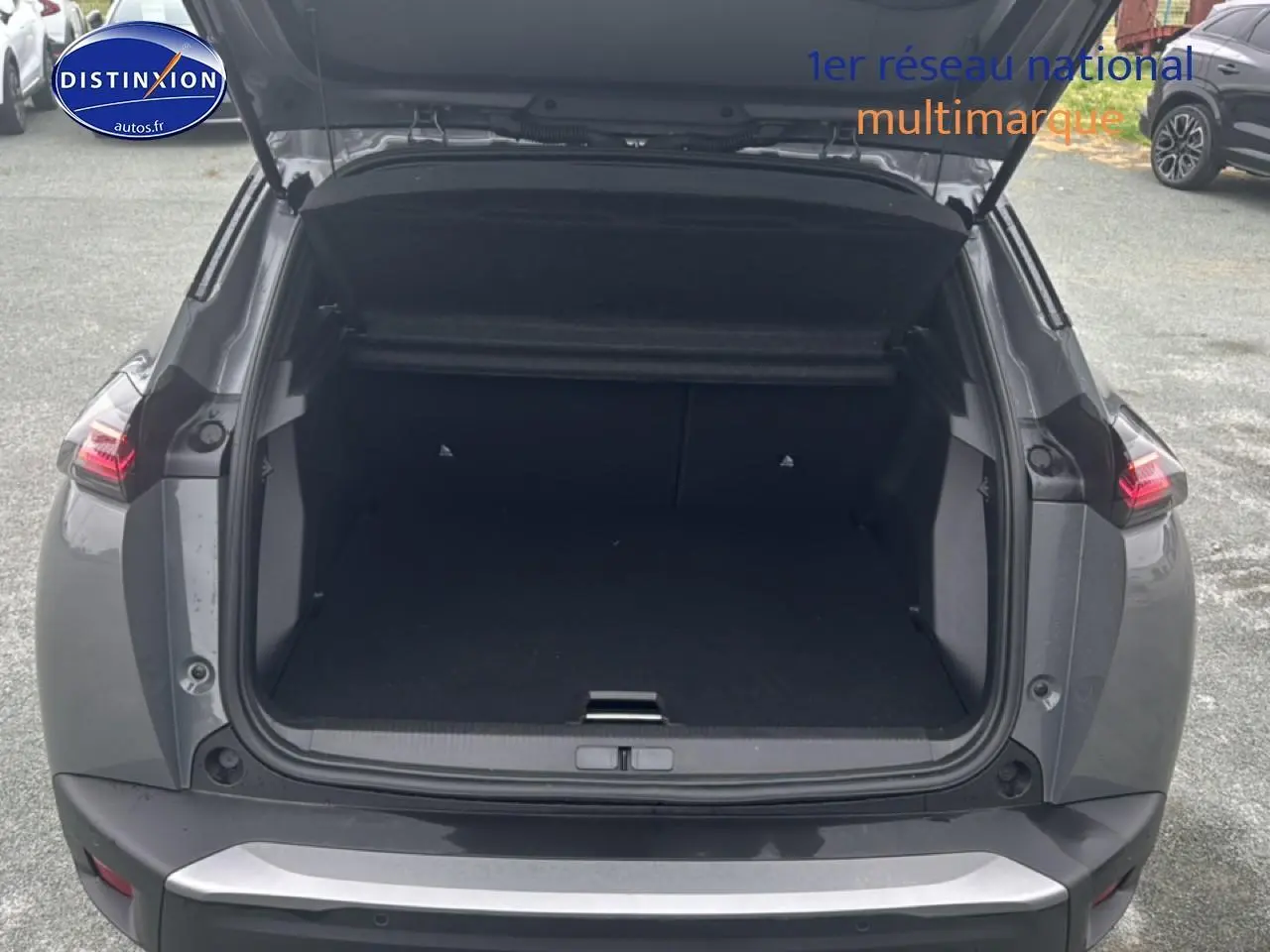 Coffre ouvert vu de l'arrière d'un Peugeot 2008 gris sélénite avec feux arrière LED allumés.