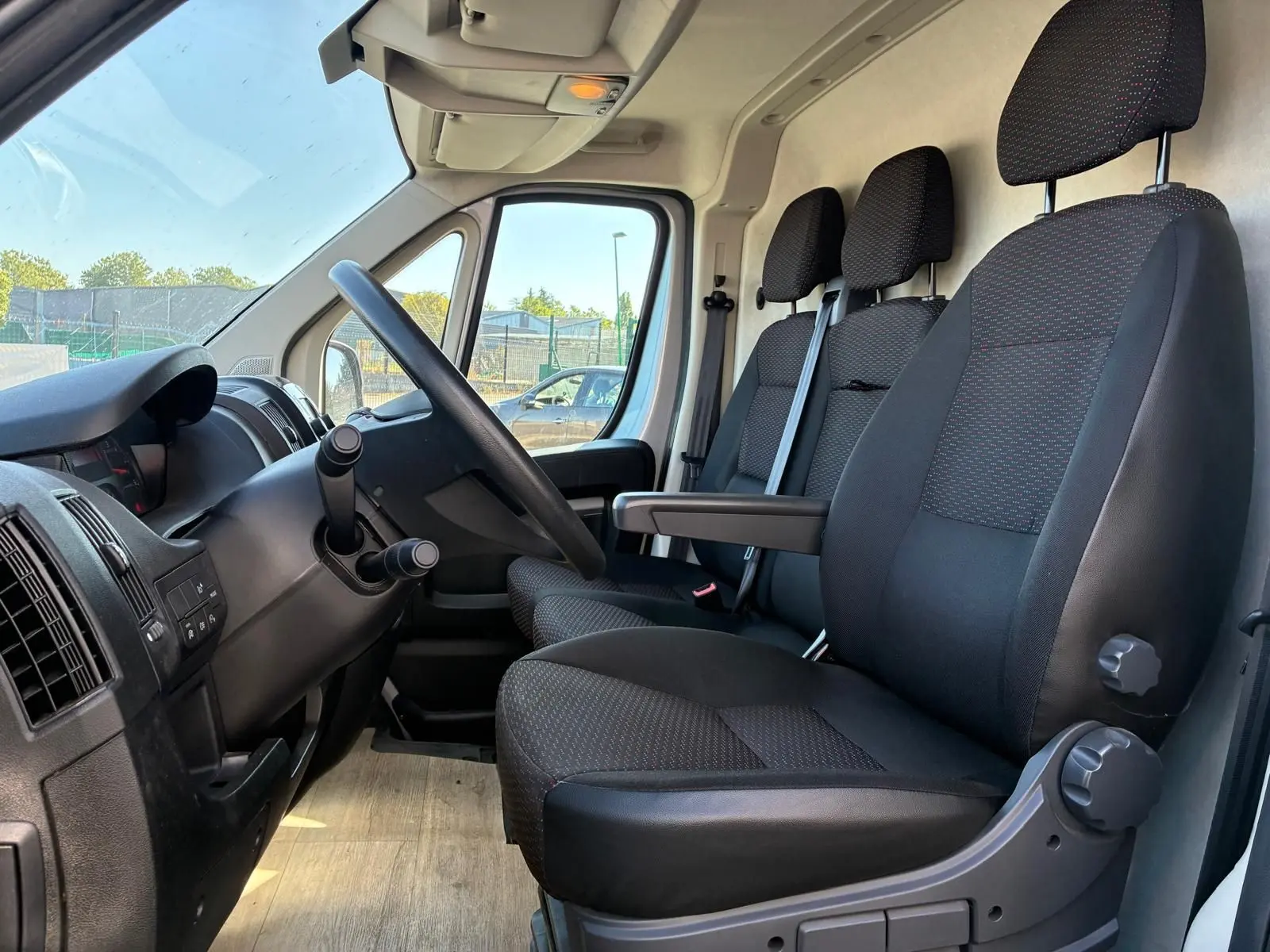 Vue intérieure côté conducteur du Peugeot Boxer cabine approfondie 2019, sièges noirs en tissu avec accoudoir central.