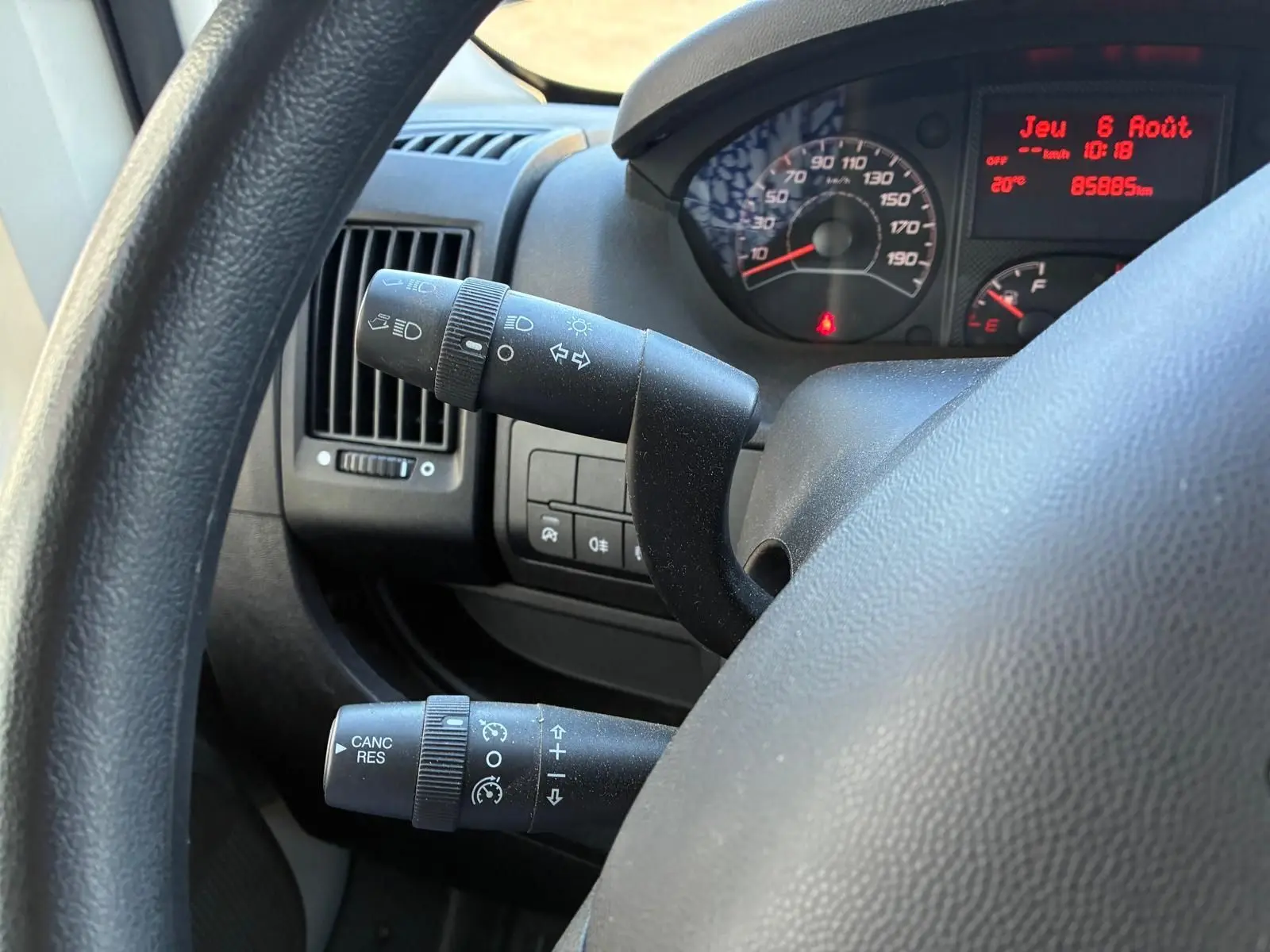 Gros plan sur le volant et les commandes du tableau de bord du Peugeot Boxer cabine approfondie gris, avec compteur et affichage digital rouge.