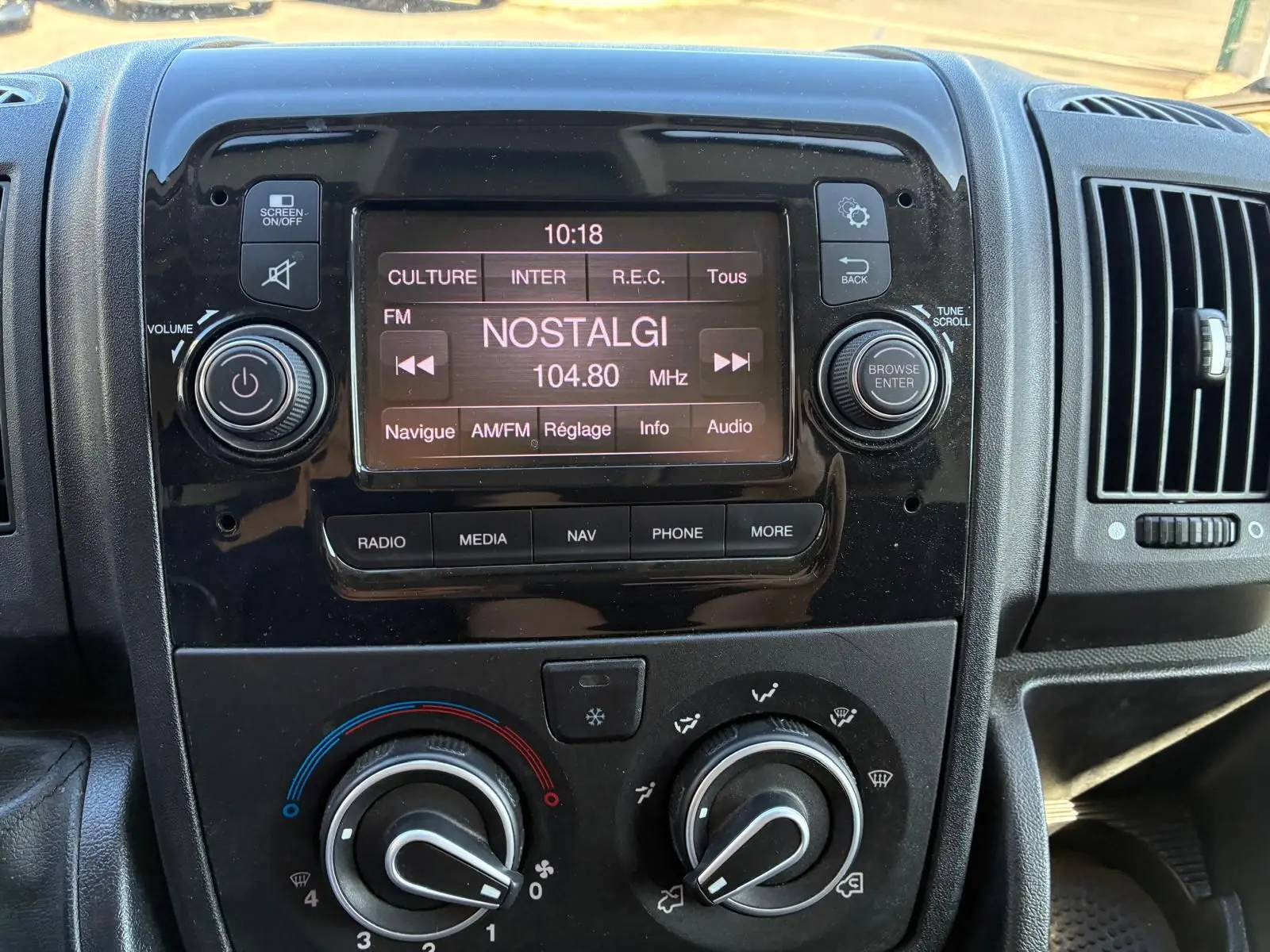 Vue rapprochée du tableau de bord noir du Peugeot Boxer Cabine Approfondie 2019 avec écran radio affichant la station Nostalgie.