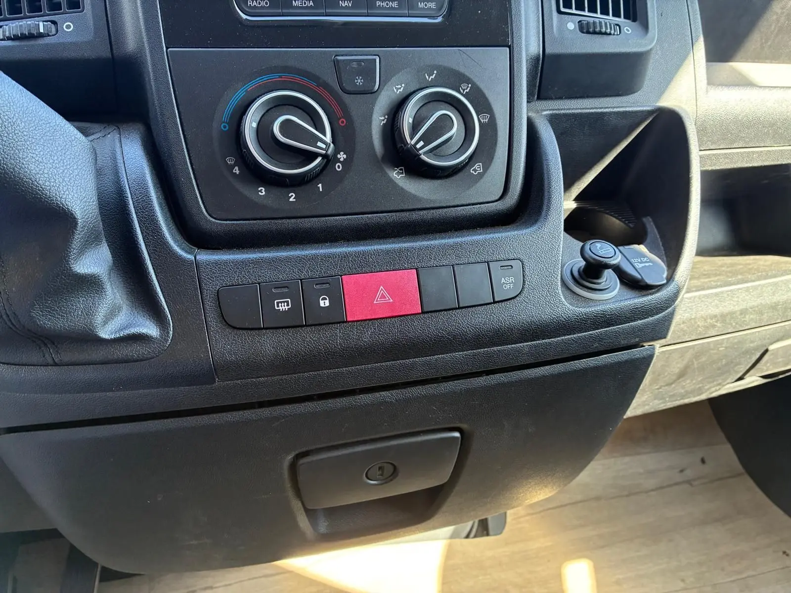 Vue rapprochée du tableau de bord gris du Peugeot Boxer cabine approfondie 2019, avec commandes clim et boutons rouges d’alerte.