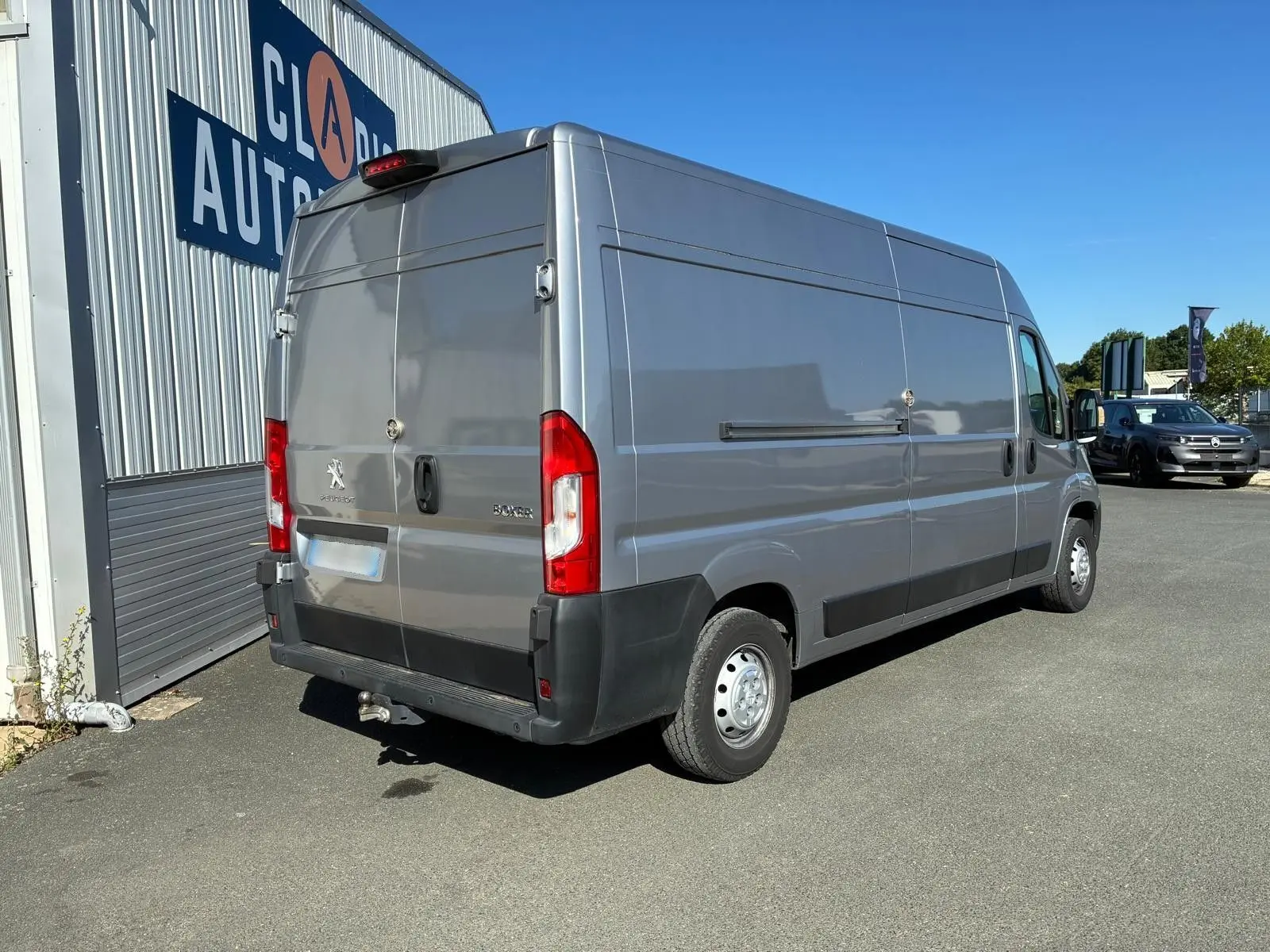 Peugeot Boxer cabine approfondie gris, vue 3/4 arrière droit, avec attelage et feux arrière rouges visibles.