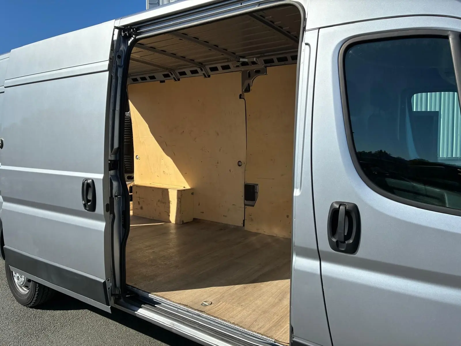Vue latérale droite d’un Peugeot Boxer gris 2019 avec porte coulissante ouverte montrant l’intérieur en bois clair.