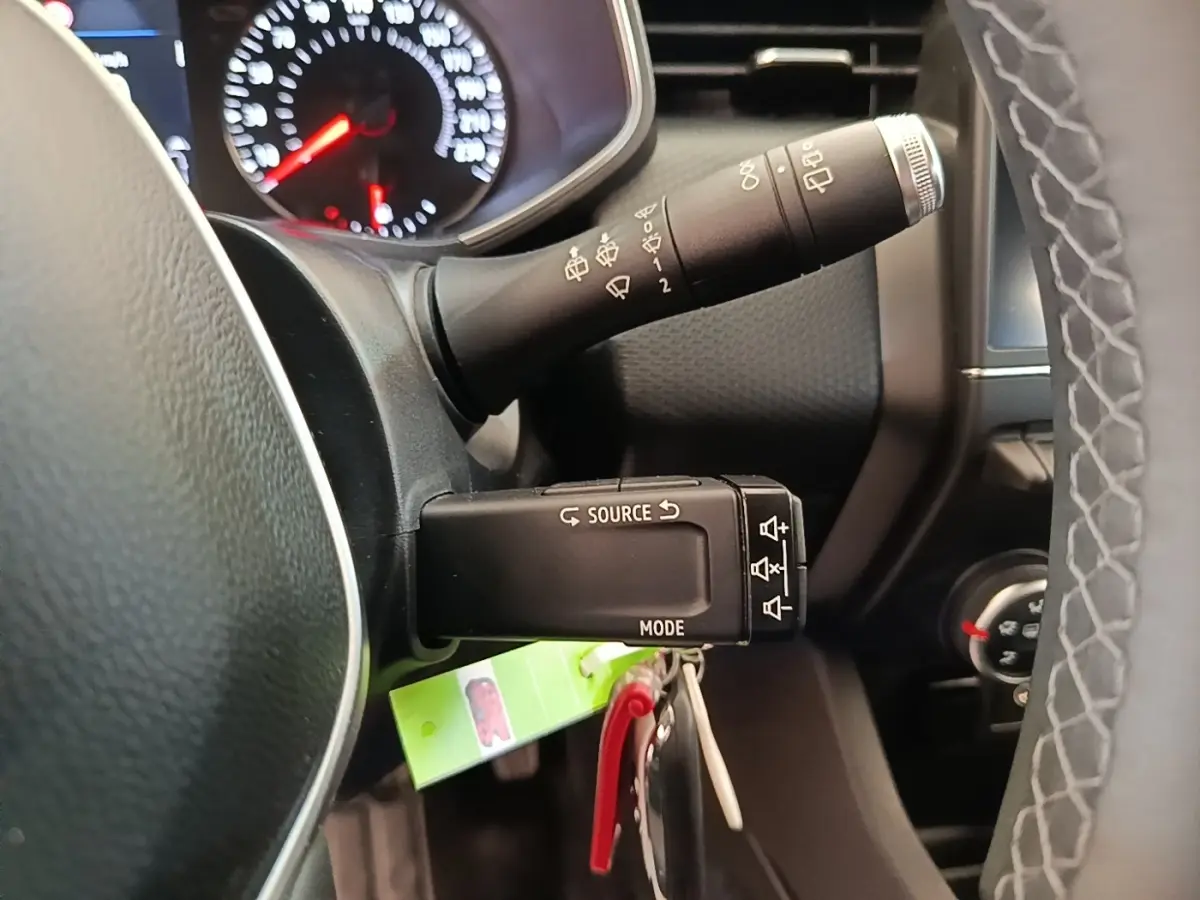 Gros plan sur la commande multifonctions noire côté gauche du volant cuir synthétique de la Renault Clio blanche, tableau de bord en arrière-plan.