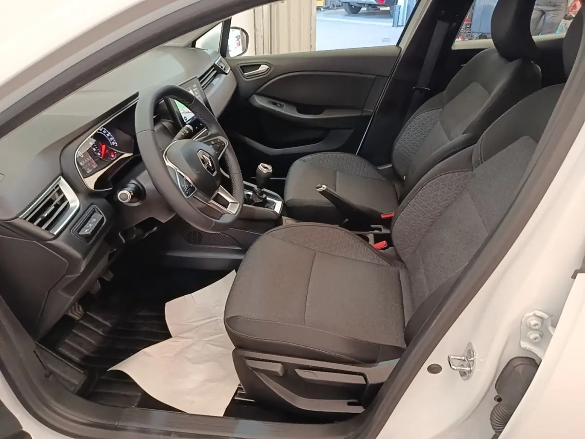 Vue intérieure côté conducteur d'une Renault Clio blanche 2020, volant multifonctions cuir et sièges tissu gris.