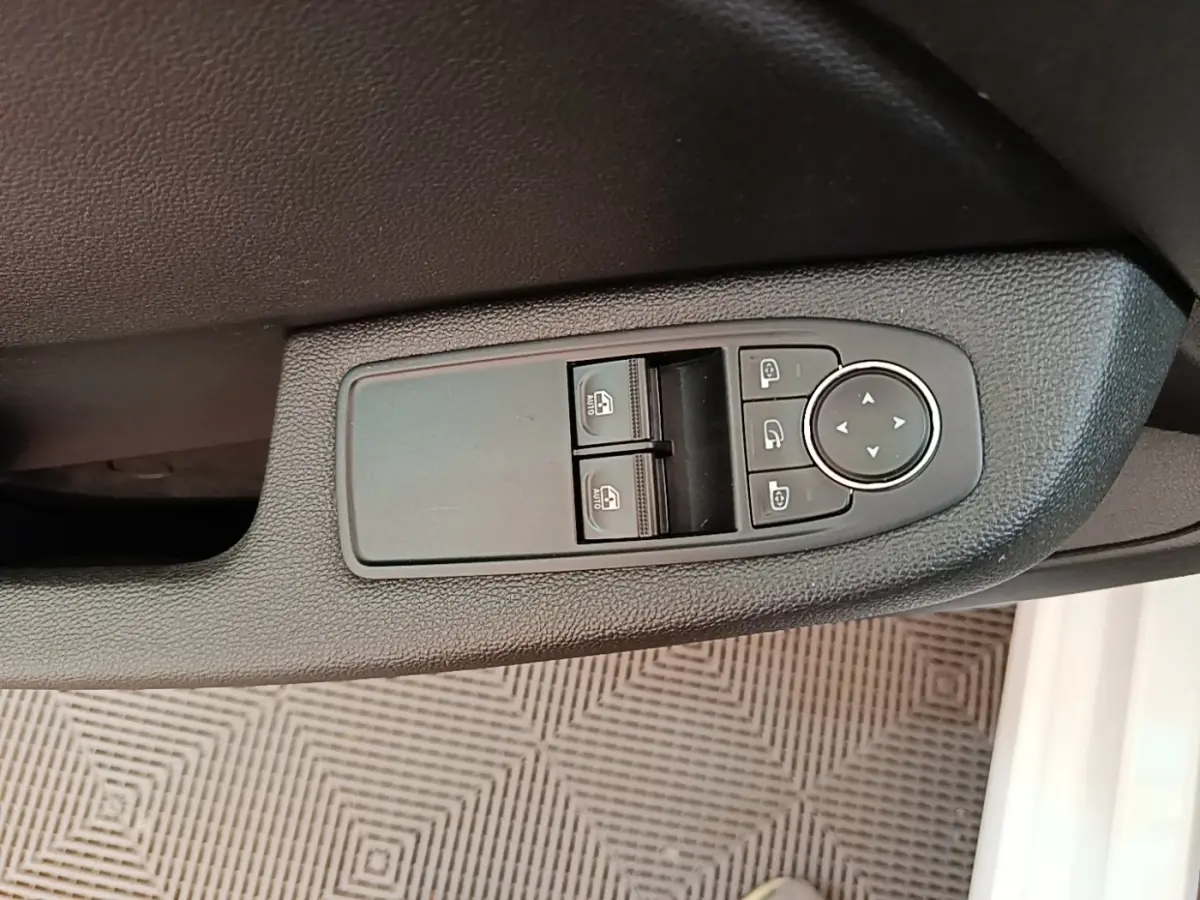 Gros plan sur les commandes de lève-vitres et rétroviseurs côté conducteur d'une Renault Clio blanche, intérieur noir.