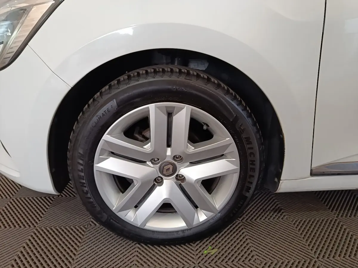 Gros plan sur la roue avant droite d'une Renault Clio blanche, jante alliage à cinq branches doubles.