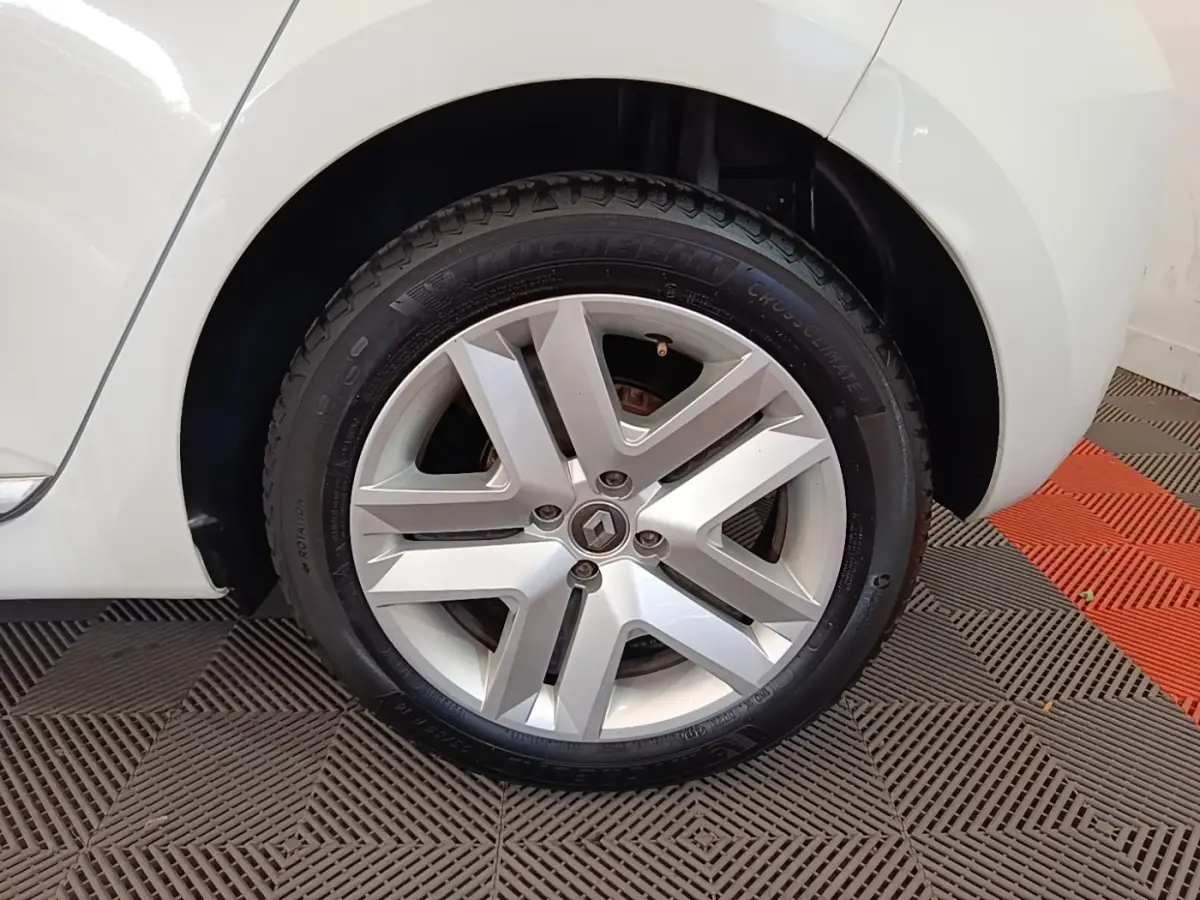 Gros plan sur la roue avant gauche d'une Renault Clio blanche, avec jante alliage et logo Renault central.