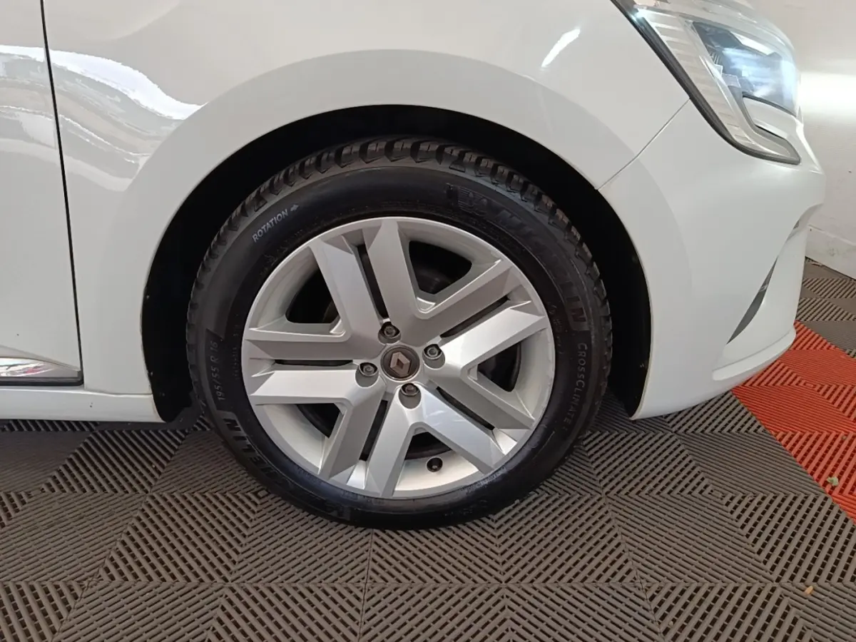 Gros plan sur la roue avant droite d’une Renault Clio blanche 2020 avec jante alliage et partie du phare avant visible.