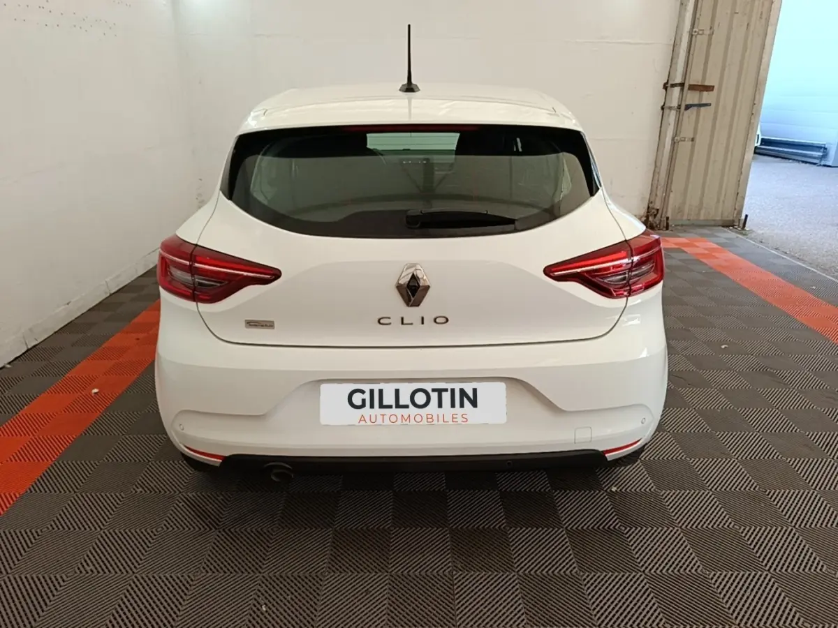 Vue arrière d'une Renault Clio blanche 2020, avec feux LED et logo distinctif sur un sol à motifs gris et orange.