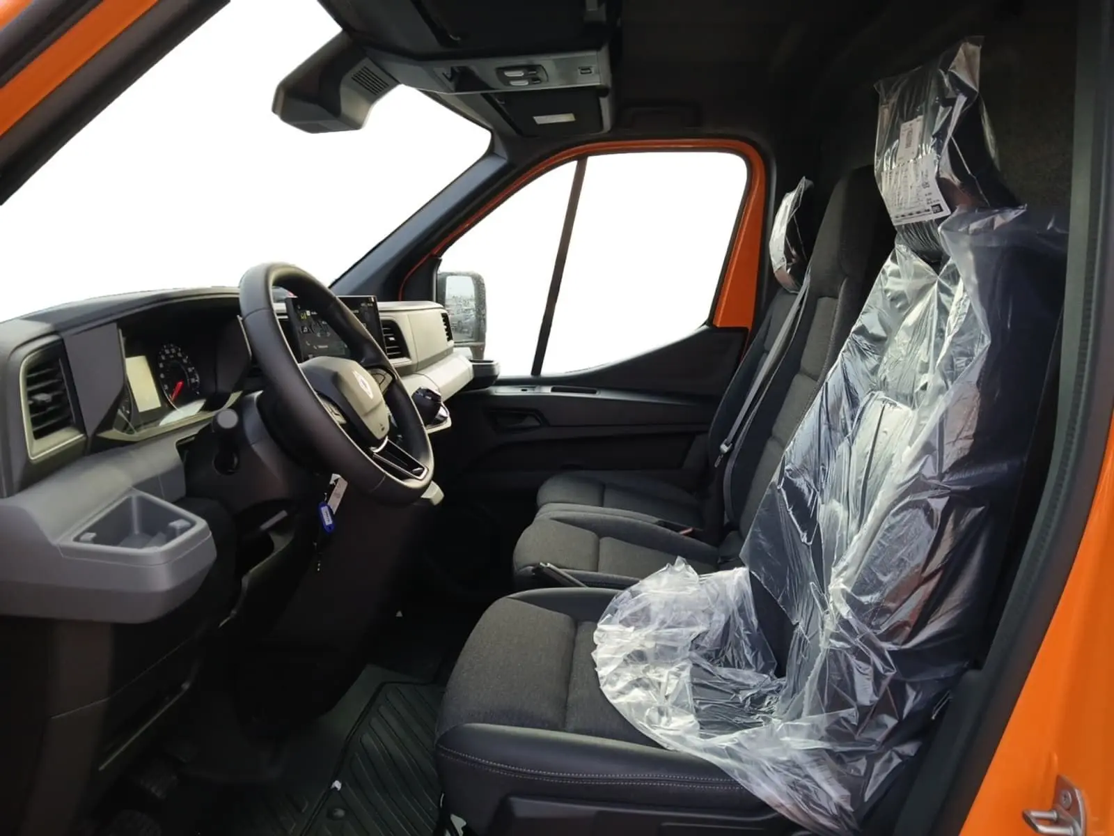 Vue intérieure côté conducteur du Renault Master orange 2026, montrant le tableau de bord et les sièges avant protégés par des housses plastiques.