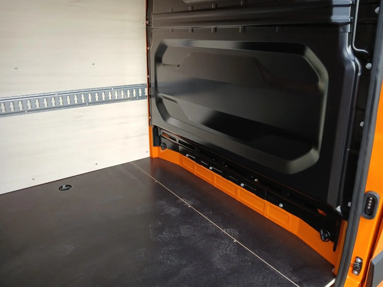 Intérieur de la zone de chargement du Renault Master orange, vue depuis l'arrière avec parois en bois clair et sol noir.