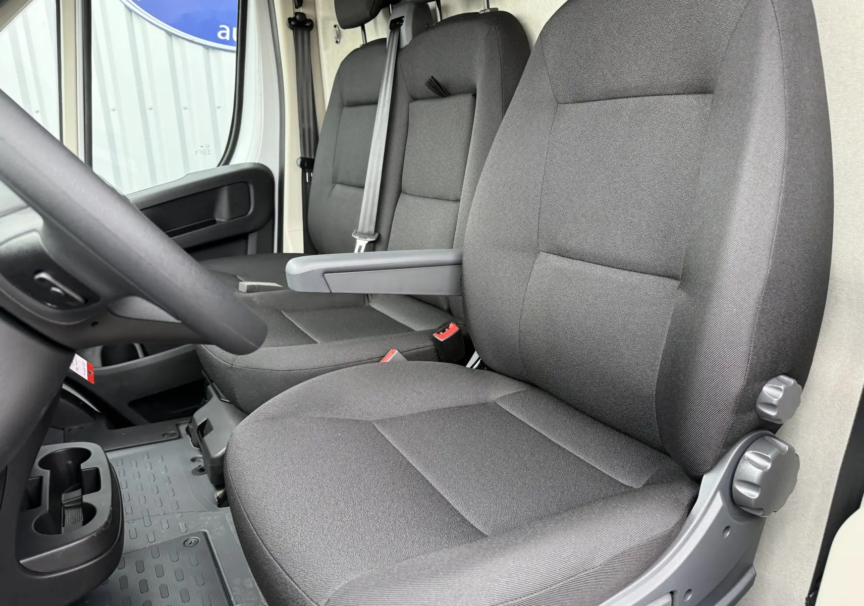 Vue intérieure côté conducteur du Citroën Jumper L3H2 2025, sièges tissu gris foncé et accoudoir central.