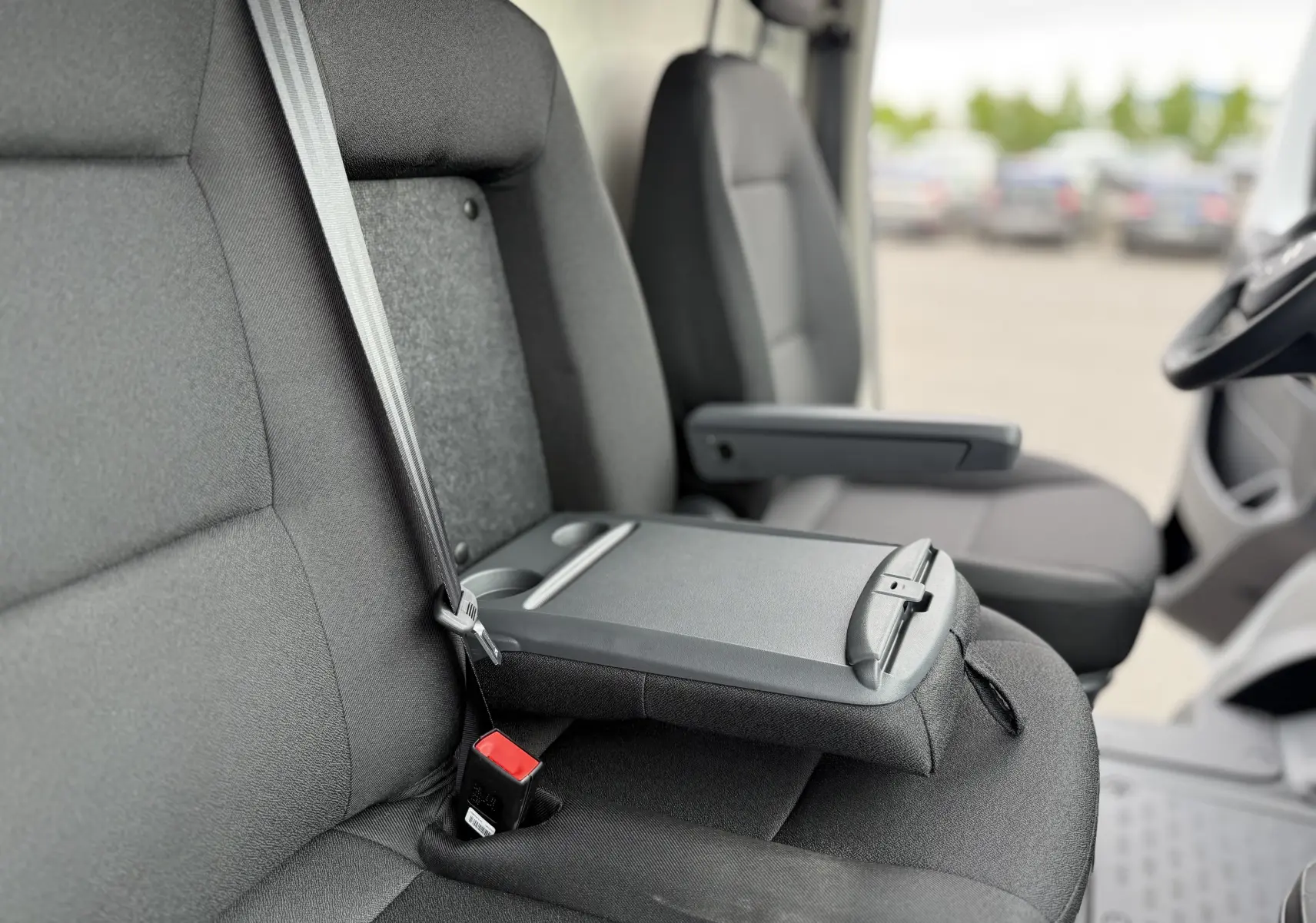 Gros plan sur les sièges avant gris foncé du Citroën Jumper L3H2 2025 avec accoudoir central et ceinture de sécurité.