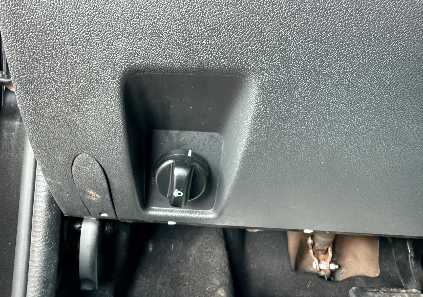 Gros plan sur le bouton de réglage des phares sous le tableau de bord d'un Dacia Duster noir métal.