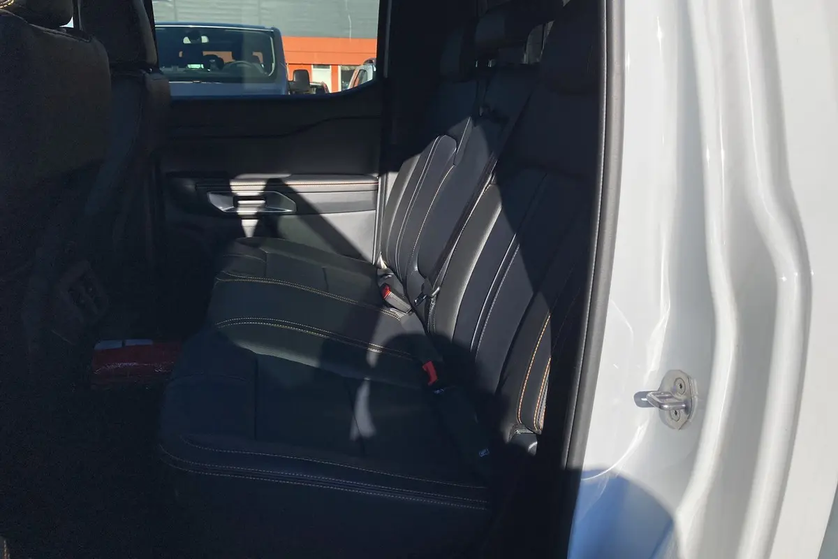 Vue intérieure côté droit sur les sièges arrière en cuir noir avec surpiqûres orange du Ford Ranger blanc glacier 2025 Wildtrak Plus.