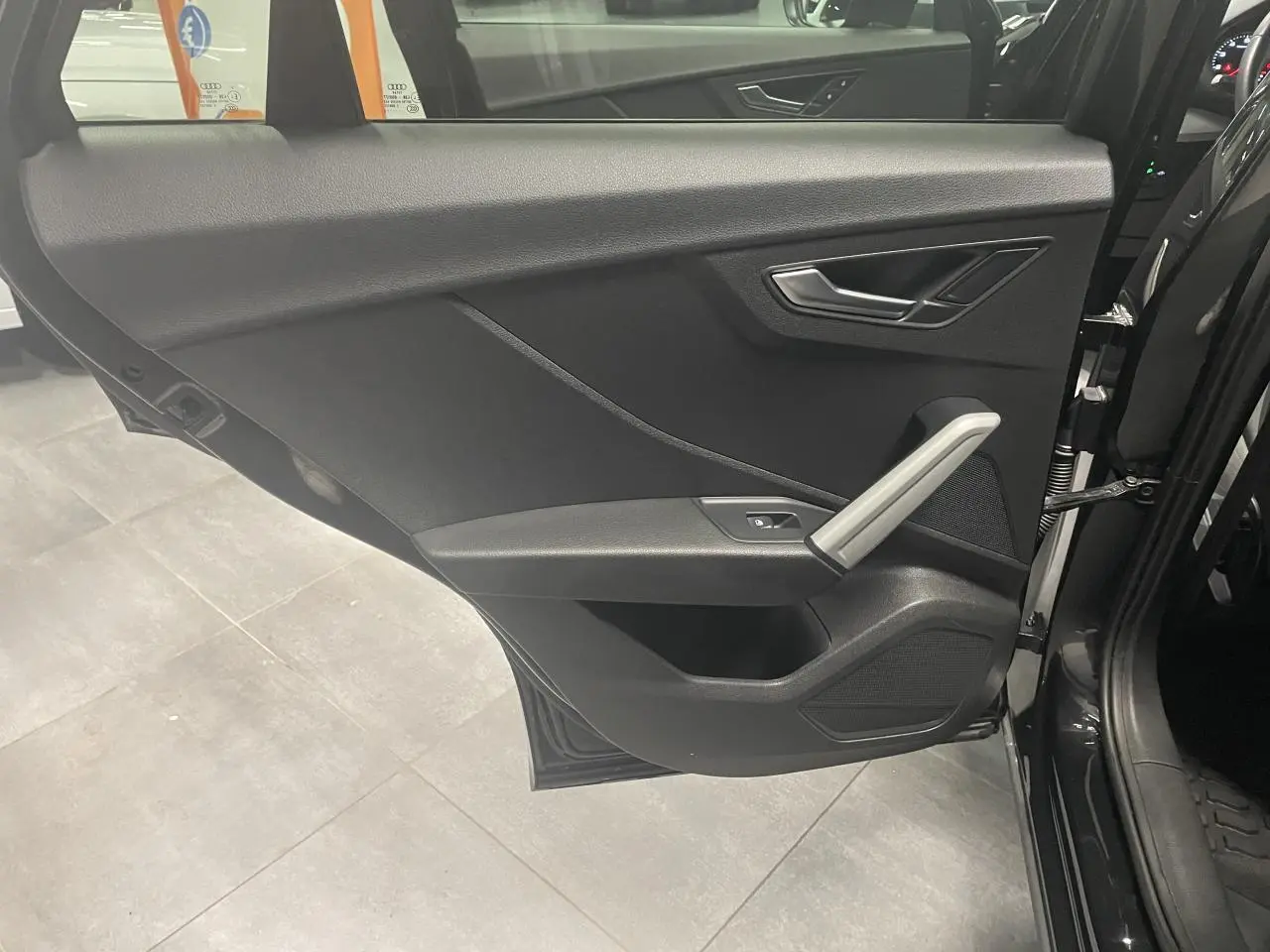 Porte avant droite ouverte d’un Audi Q2 noir métallisé, montrant le panneau intérieur noir avec poignée argentée.