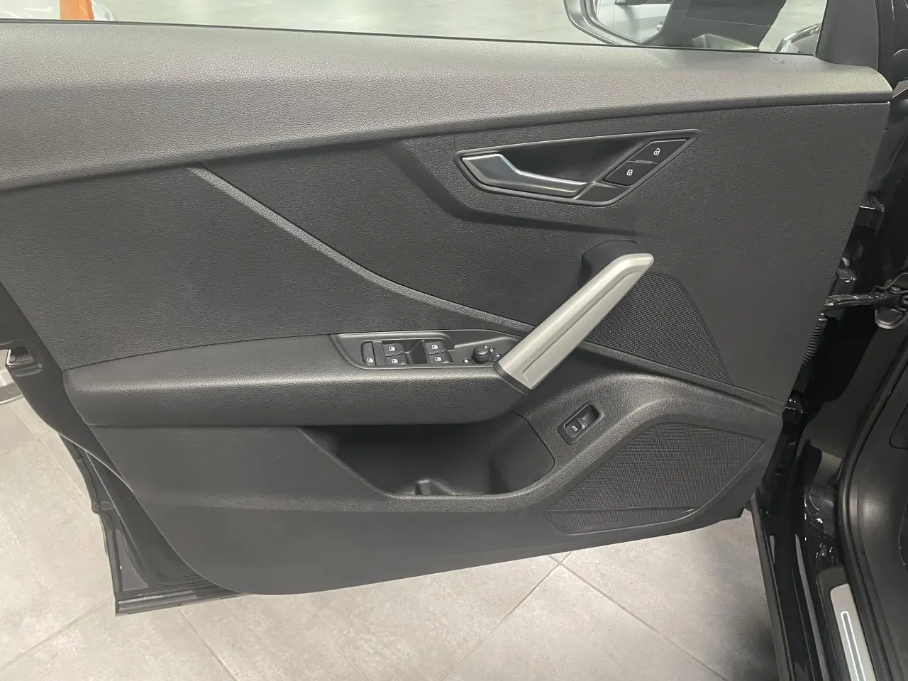 Vue intérieure de la porte avant gauche noire métallisée de l'Audi Q2 S line avec commandes de vitres et poignée aluminium.