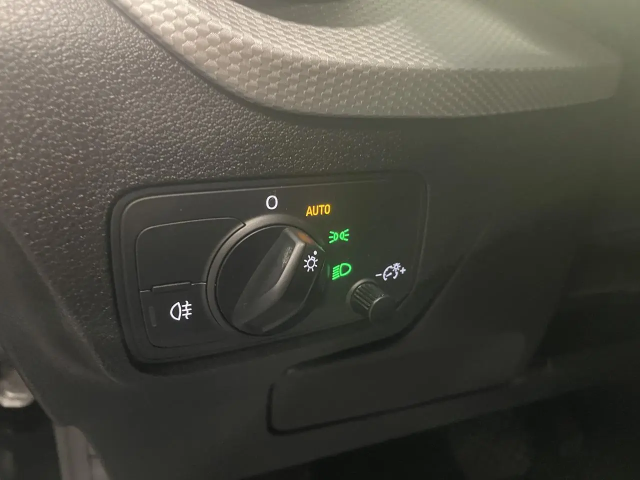 Gros plan sur la commande d’éclairage intérieure noire de l’Audi Q2, avec réglage rotatif et indicateurs lumineux verts et jaunes.