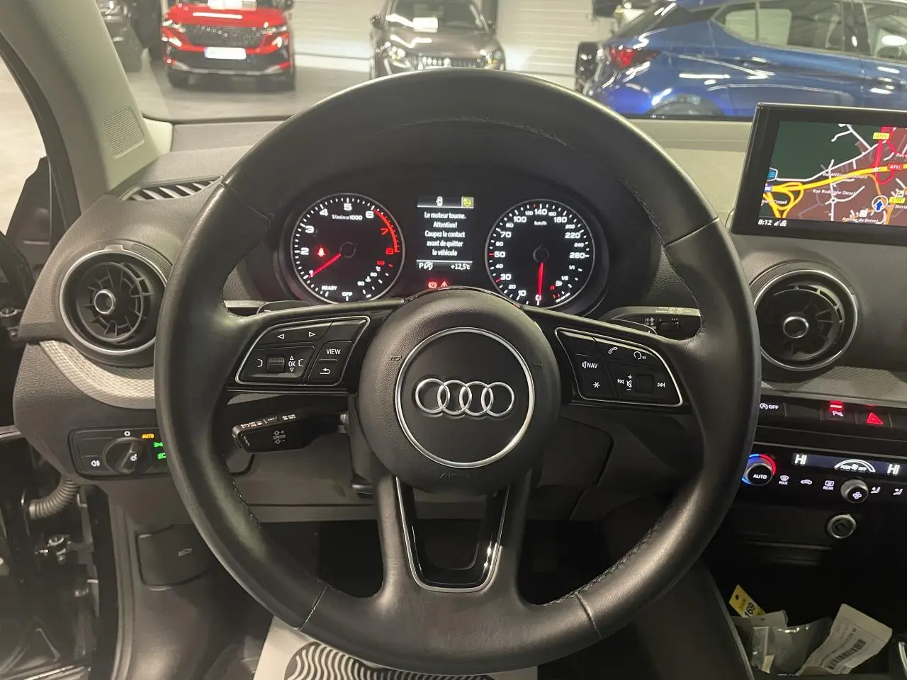 Vue intérieure centrée sur le volant cuir noir de l'Audi Q2 2023 avec tableau de bord et écran de navigation visibles.