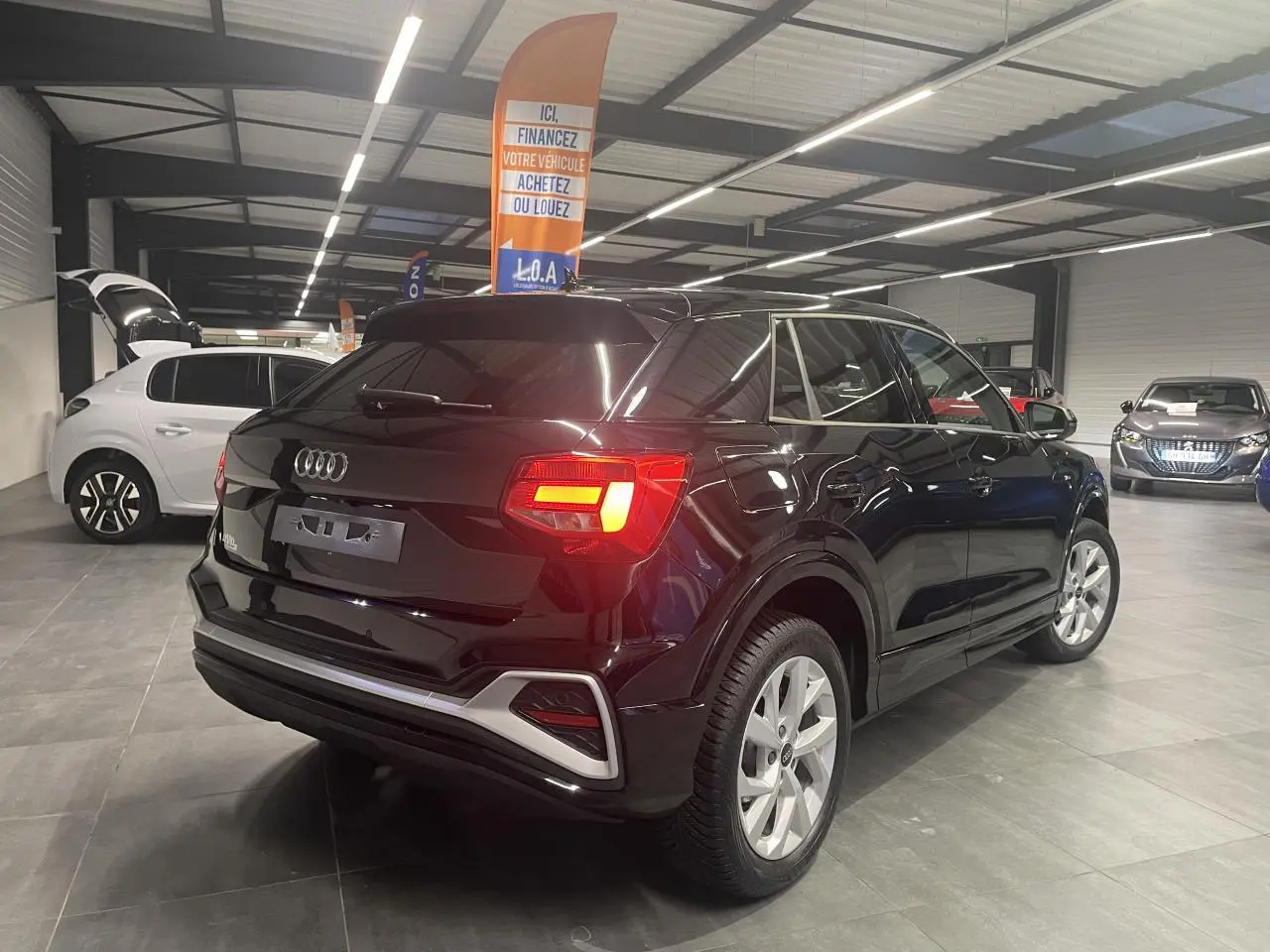Vue 3/4 arrière droit d’un Audi Q2 noir métallisé avec feux arrière LED allumés en intérieur showroom.