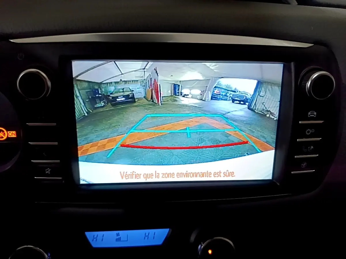 Vue de l'écran de caméra de recul de la Toyota Yaris blanche, affichant les lignes de guidage dans un garage.