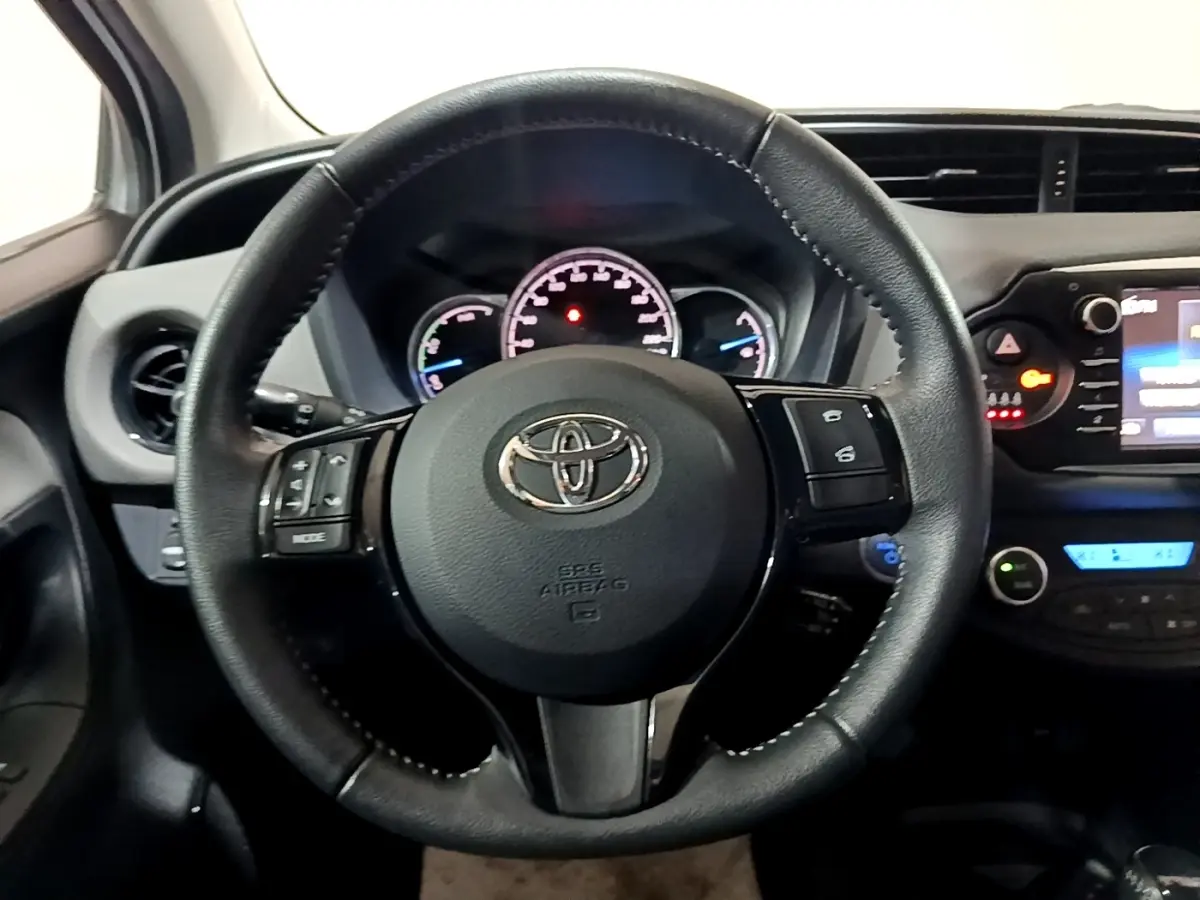 Vue intérieure centrée sur le volant cuir et alu multifonctions de la Toyota Yaris hybride 2019, tableau de bord visible.