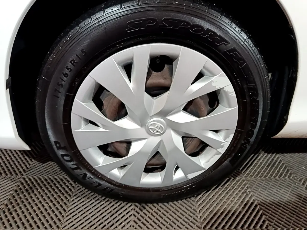 Gros plan sur la roue avant gauche blanche d'une Toyota Yaris 1.5 VVT-I Hybrid avec enjoliveur argenté marqué Toyota.