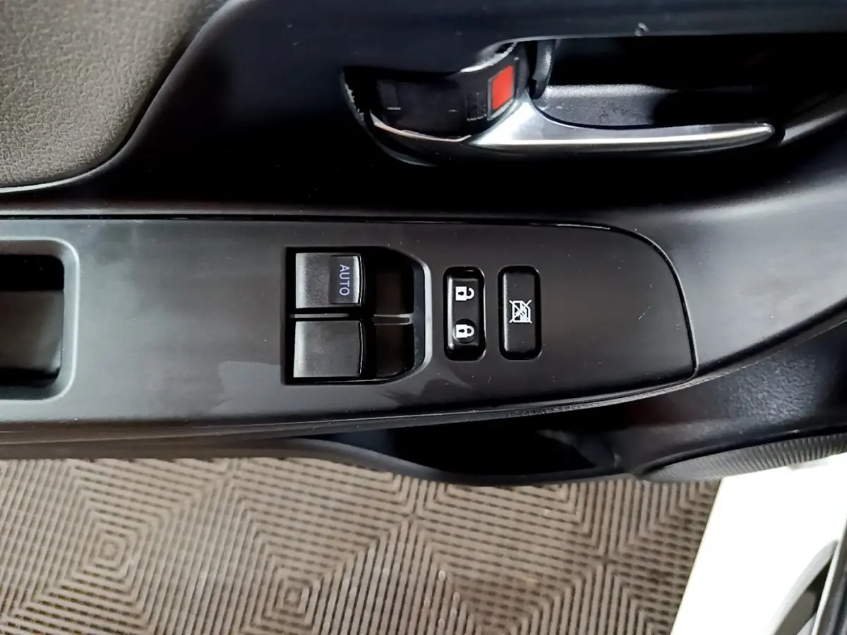 Gros plan sur les commandes de porte côté conducteur d'une Toyota Yaris blanche, avec boutons de verrouillage et lève-vitres.
