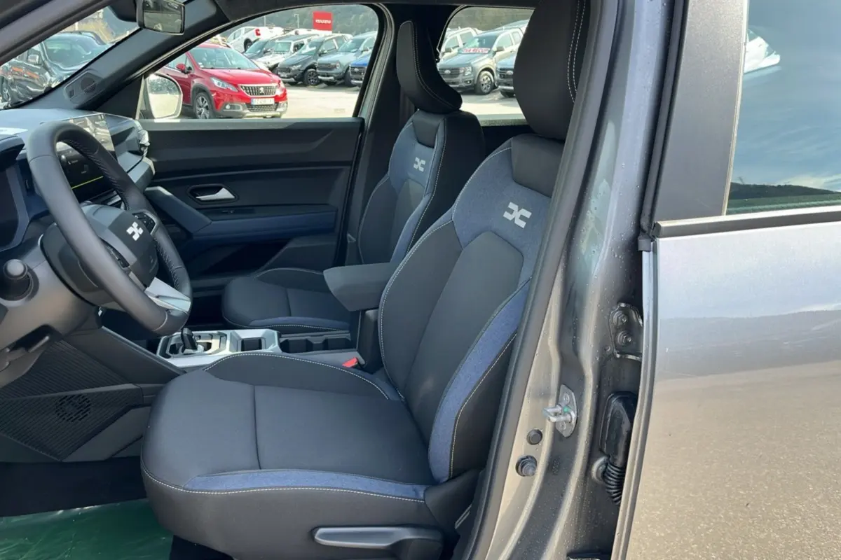 Vue intérieure côté conducteur du Dacia Bigster Hybrid 155 Expression Plus gris schiste, sièges tissu avec logo distinctif.