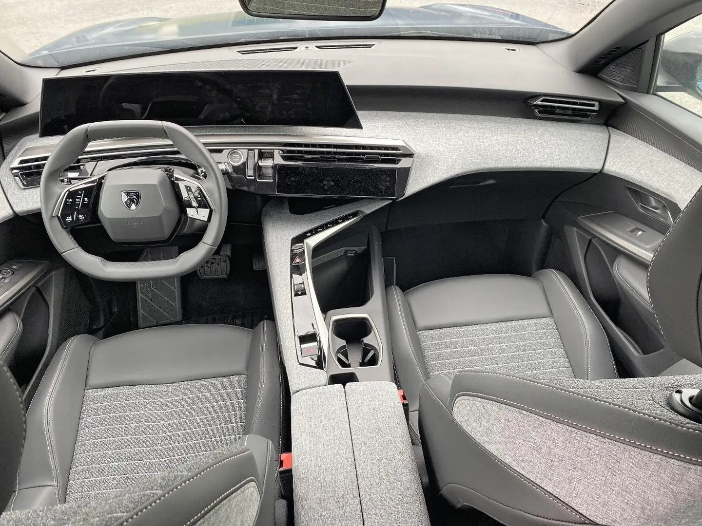 Vue intérieure avant du Peugeot 3008 2025, volant compact, tableau de bord numérique et sellerie gris clair et noir.