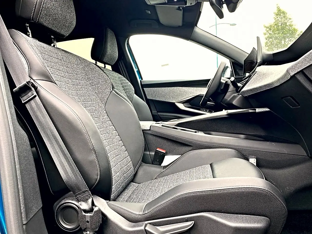 Vue intérieure côté conducteur du Peugeot 3008 2025 bleu, sièges tissu et cuir gris avec console centrale moderne.