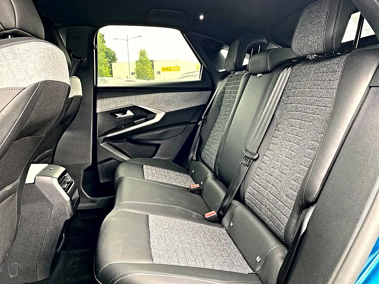 Vue intérieure arrière droite des sièges en tissu gris et cuir noir du Peugeot 3008 1.2 hybrid 145 allure bleu 2025.