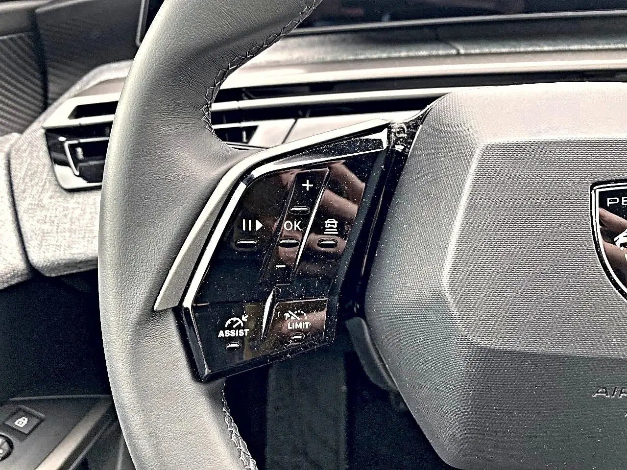 Gros plan sur le côté gauche du volant cuir Peugeot 3008 2025 avec commandes multifonctions et logo central.