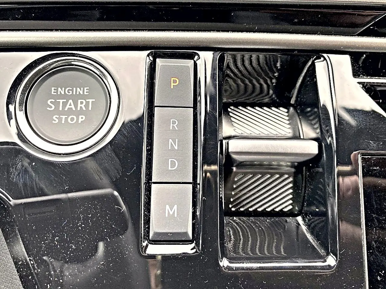 Gros plan sur la console centrale noire brillante du Peugeot 3008 1.2 hybrid 145 allure e-dcs6 avec bouton start/stop et sélecteur de vitesses automatique.