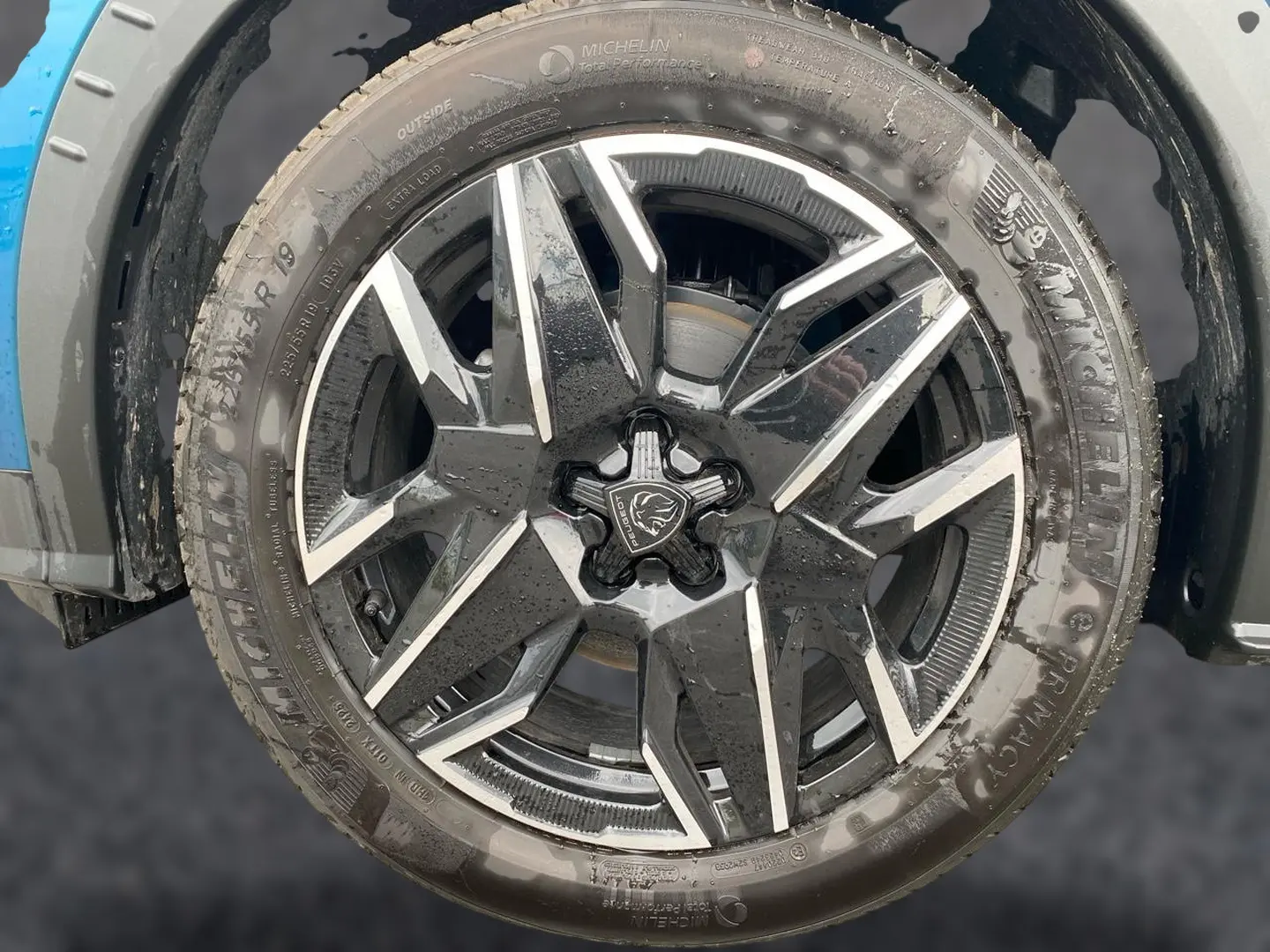 Gros plan sur la jante alu noire et argentée d’un Peugeot 3008 bleu, montrant le logo lion central.