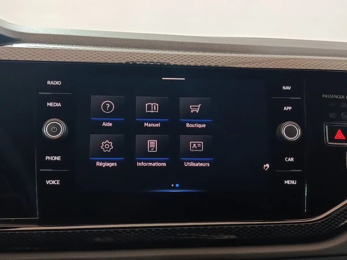 Écran tactile central de la Volkswagen Polo gris foncé, affichant le menu principal avec options d’aide et réglages.