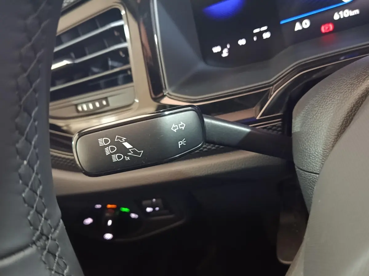 Gros plan sur le commodo gauche du volant d’une Volkswagen Polo gris foncé, avec tableau de bord numérique en arrière-plan.