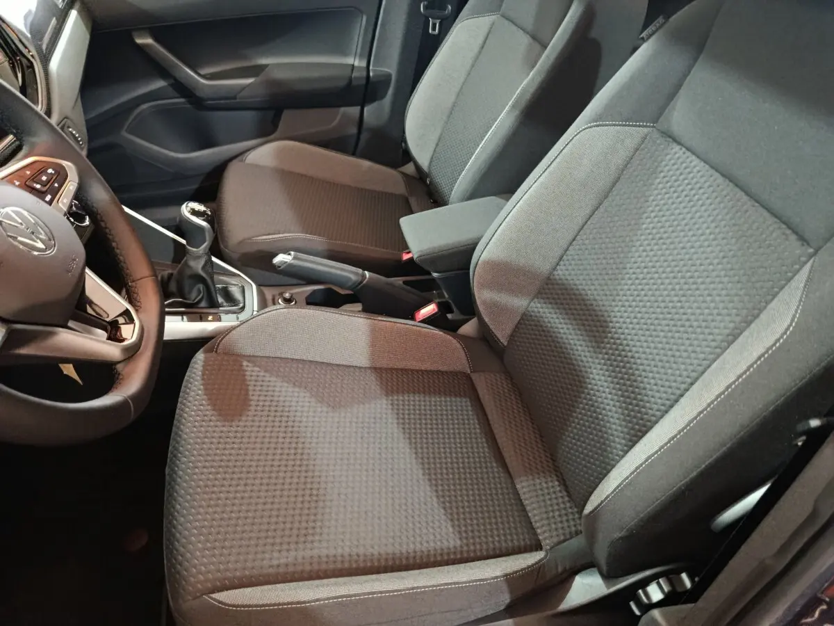 Vue intérieure côté conducteur de la Volkswagen Polo gris foncé 2025, montrant sièges tissu et levier de vitesses manuel.