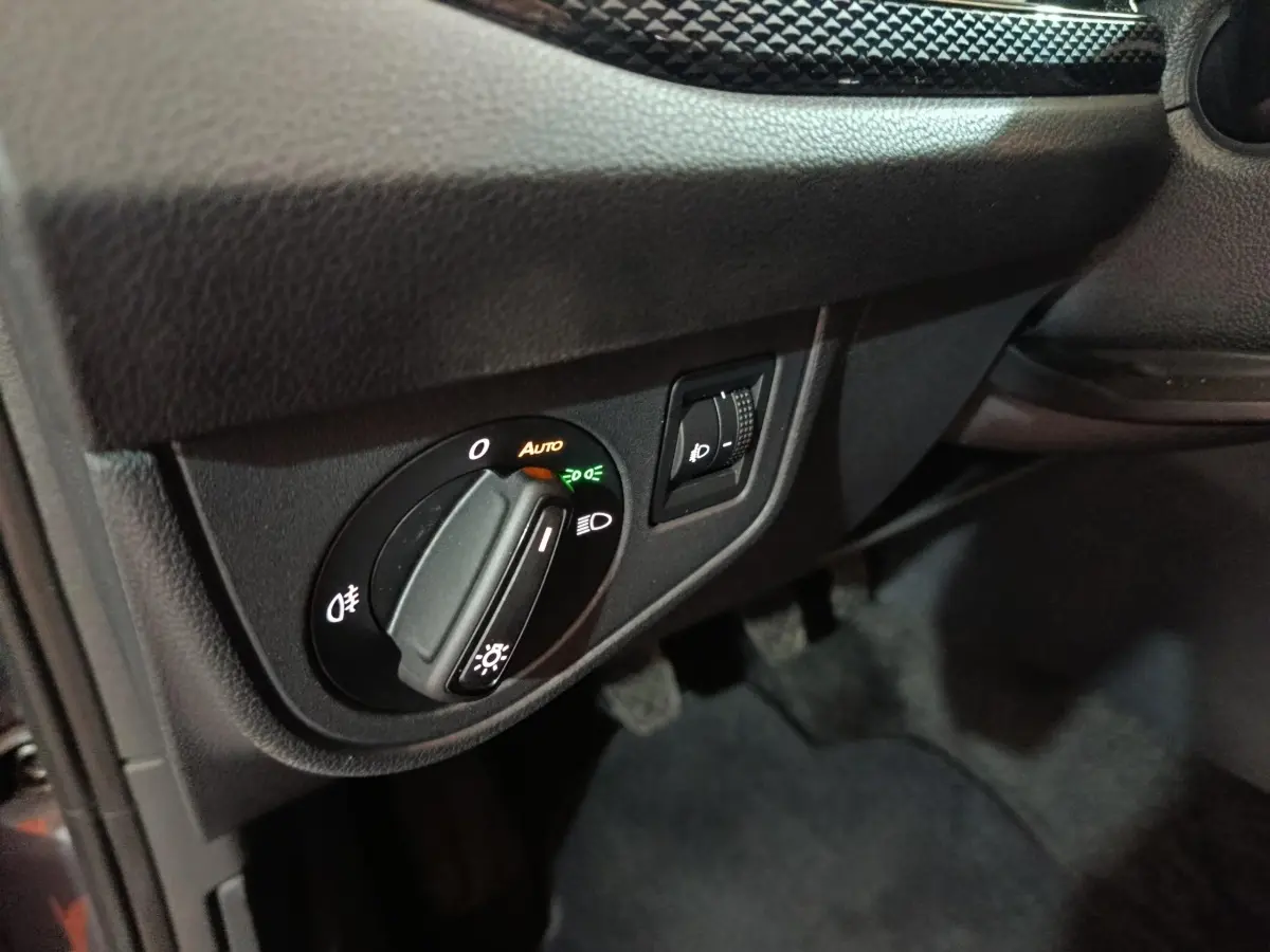 Gros plan sur le bouton de commande des phares et réglage d’intensité dans l’habitacle noir d’une Volkswagen Polo 2025 gris foncé.