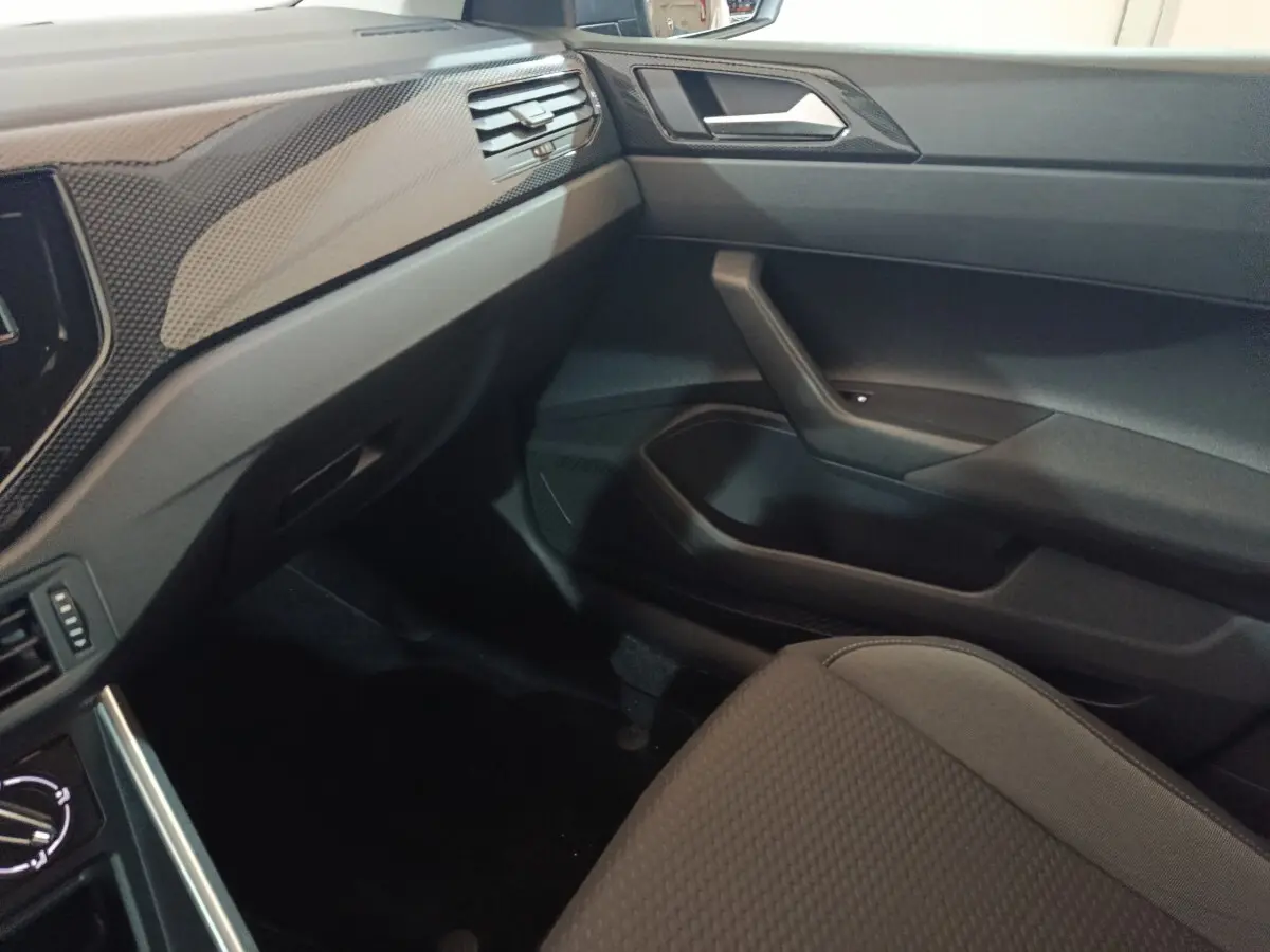 Vue intérieure côté passager de la Volkswagen Polo 2025 gris foncé, montrant la planche de bord et la porte avec finition carbone.