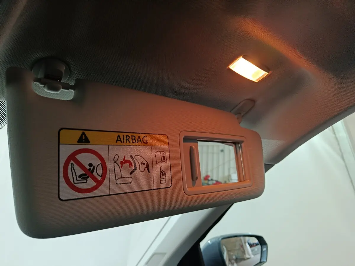 Vue intérieure du pare-soleil côté conducteur gris clair avec miroir et avertissement airbag éclairé.