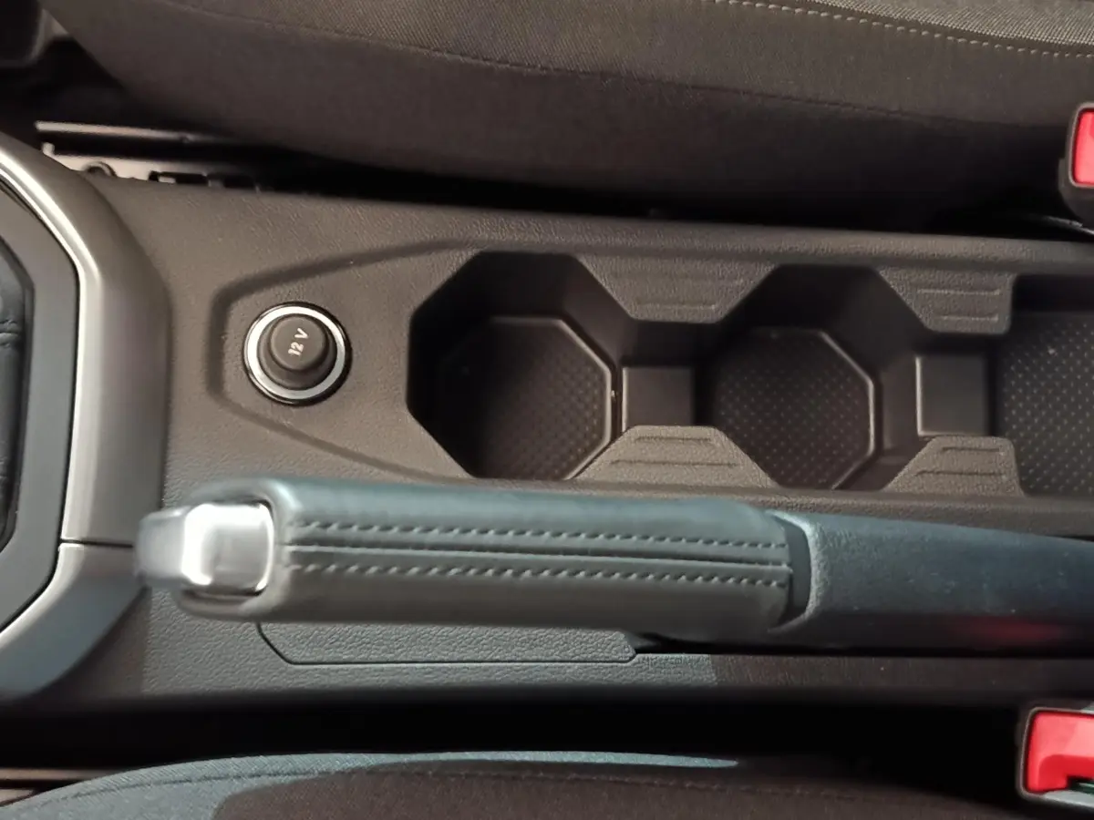 Vue rapprochée de la console centrale de la Volkswagen Polo gris foncé, avec frein à main manuel et prise 12V.