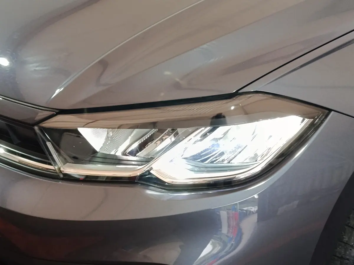 Gros plan sur le phare avant droit allumé d'une Volkswagen Polo gris foncé, mettant en valeur ses lignes modernes.