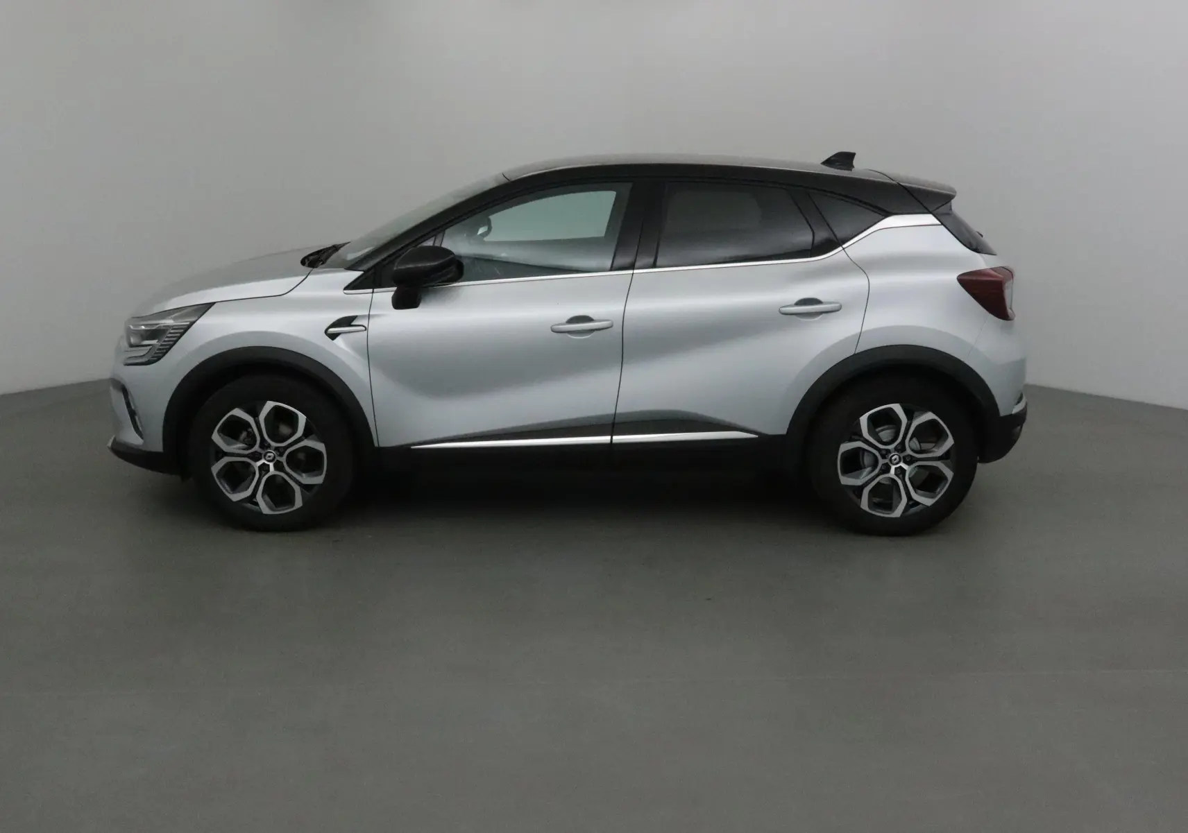 Profil côté gauche d'un Renault Captur 2024 gris Highland avec toit noir et jantes 18 pouces en alliage.