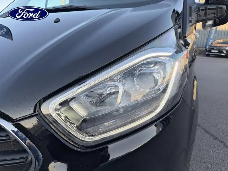 Gros plan sur le phare avant droit du Ford Transit Custom noir Agate métallisé, soulignant ses lignes modernes et précises.