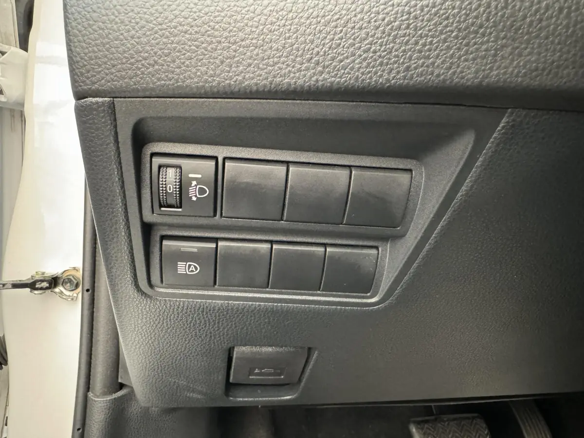 Gros plan sur les commandes de réglage des phares et fonction auto, côté gauche d’une Toyota Yaris blanche 2022.